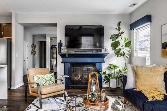 living area with a glass covered fireplace, visible vents, baseboards, and wood finished floors