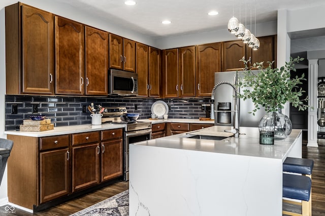 kitchen with backsplash, dark wood finished floors, a breakfast bar area, light countertops, and appliances with stainless steel finishes