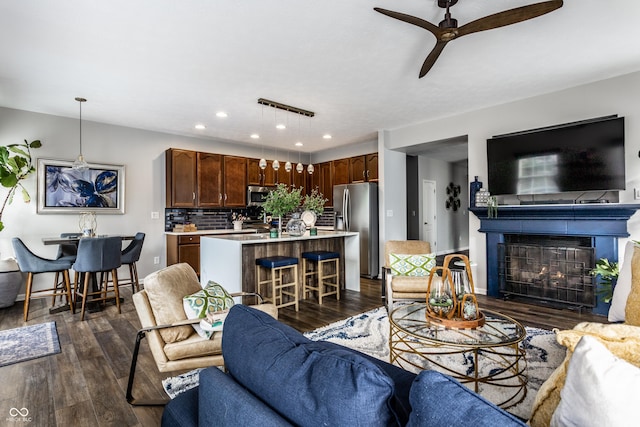 living room featuring a glass covered fireplace, baseboards, dark wood finished floors, and a ceiling fan