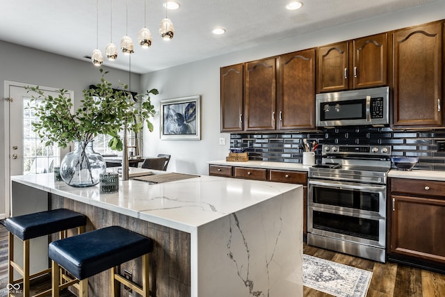 kitchen featuring backsplash, a kitchen island, light stone counters, stainless steel appliances, and dark wood-style flooring