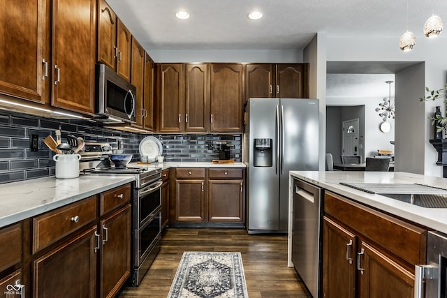 kitchen with light stone countertops, dark wood finished floors, stainless steel appliances, decorative backsplash, and decorative light fixtures