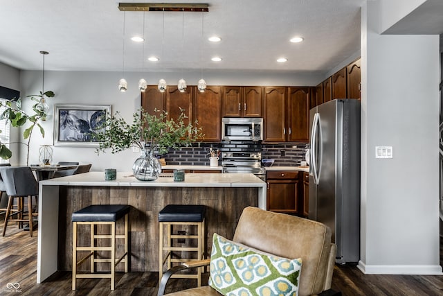 kitchen featuring light countertops, dark wood-type flooring, appliances with stainless steel finishes, tasteful backsplash, and a center island