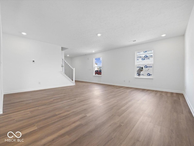 unfurnished living room with wood finished floors, baseboards, recessed lighting, stairs, and a textured ceiling