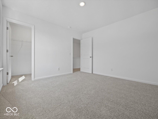 unfurnished bedroom featuring a closet, baseboards, light colored carpet, and a spacious closet