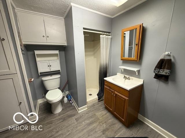 full bathroom featuring toilet, a textured ceiling, wood finished floors, a shower stall, and vanity