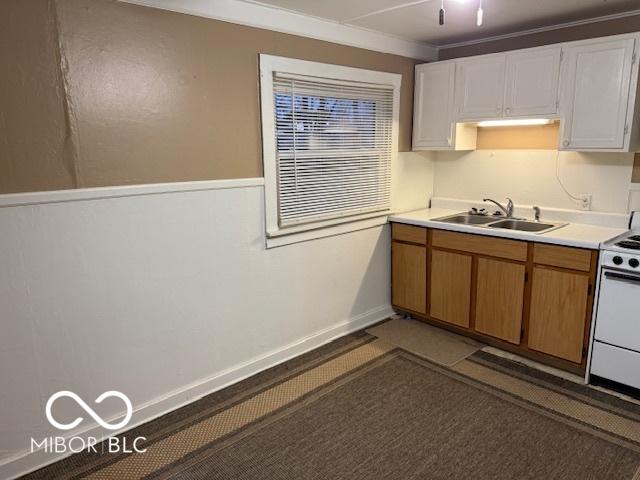 kitchen with baseboards, light countertops, white range with electric stovetop, white cabinetry, and a sink