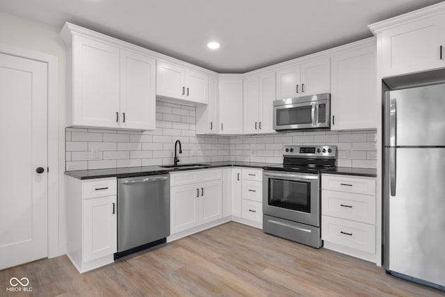 kitchen with dark countertops, stainless steel appliances, light wood-type flooring, and a sink