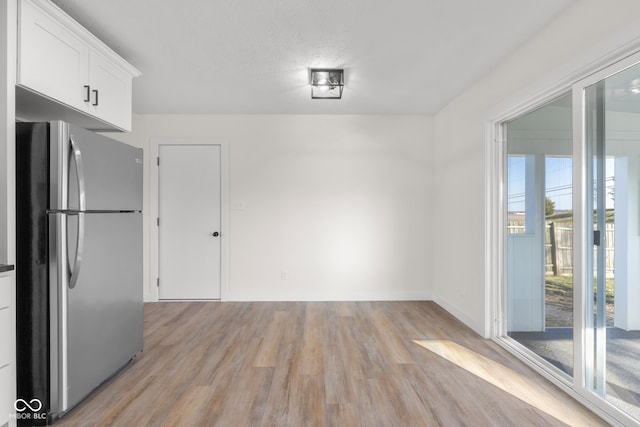 unfurnished dining area featuring baseboards, light wood-style floors, and a textured ceiling