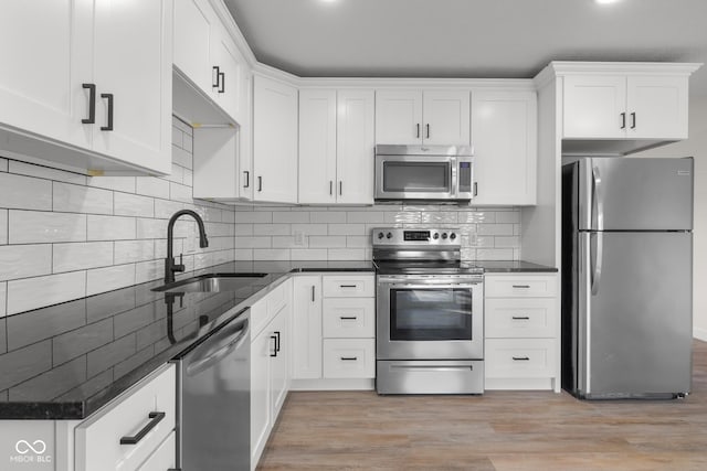 kitchen featuring light wood-type flooring, a sink, stainless steel appliances, white cabinets, and decorative backsplash