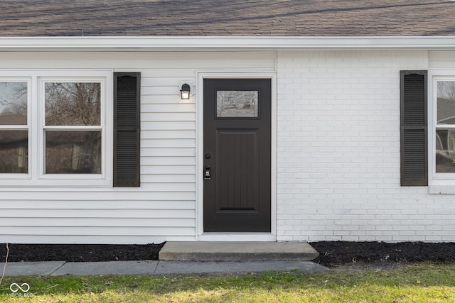 entrance to property featuring brick siding and roof with shingles