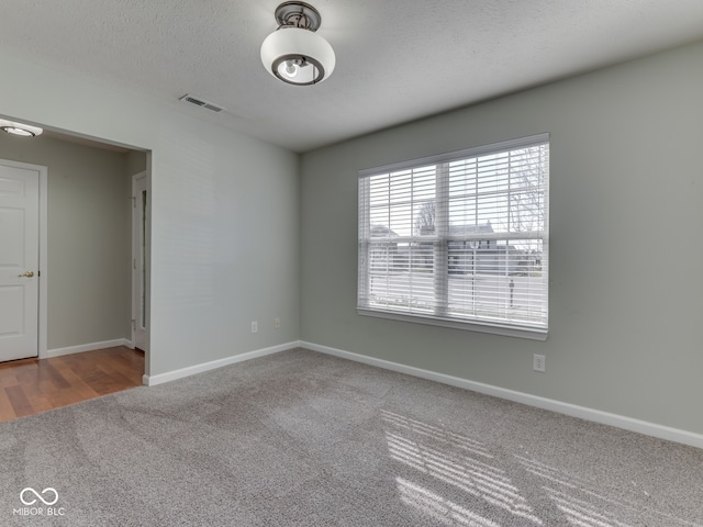 carpeted spare room with baseboards, visible vents, and a textured ceiling