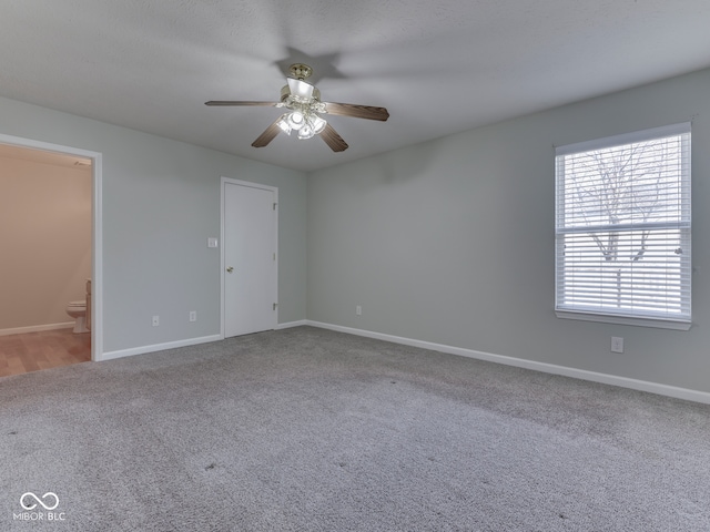 carpeted spare room with a ceiling fan and baseboards