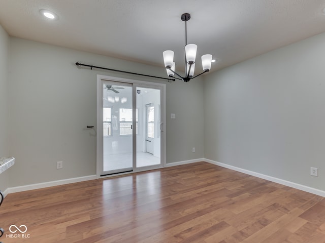 empty room featuring light wood-type flooring, baseboards, and ceiling fan with notable chandelier