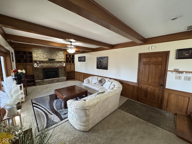 carpeted living room with beam ceiling, wainscoting, a fireplace, and ceiling fan