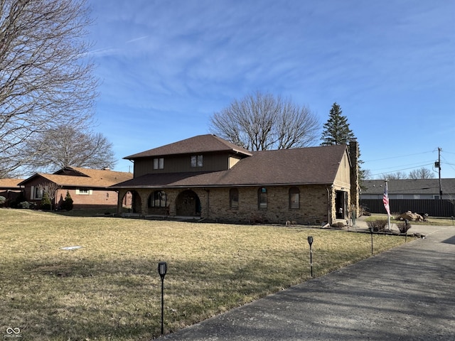 view of front of house with brick siding, a shingled roof, a front yard, and fence