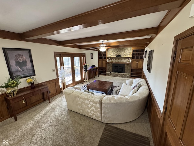 living room with beam ceiling, a stone fireplace, french doors, wainscoting, and carpet flooring