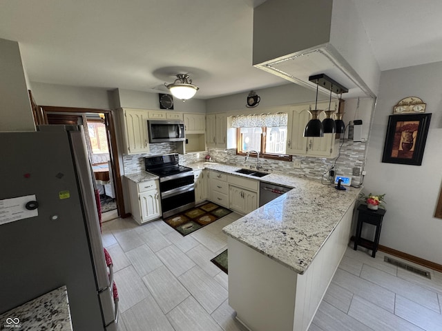 kitchen featuring visible vents, a peninsula, a sink, stainless steel appliances, and tasteful backsplash