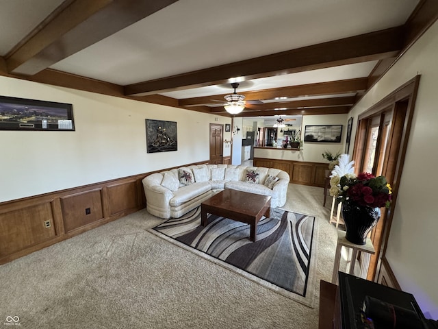 carpeted living area with beam ceiling, ceiling fan, and wainscoting