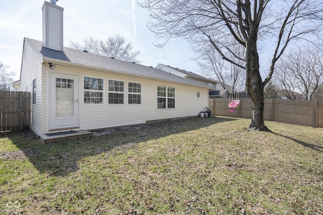 back of house with a yard, a fenced backyard, and a chimney