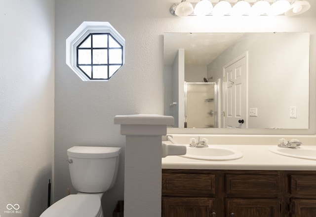 bathroom with double vanity, toilet, a shower with shower door, and a sink