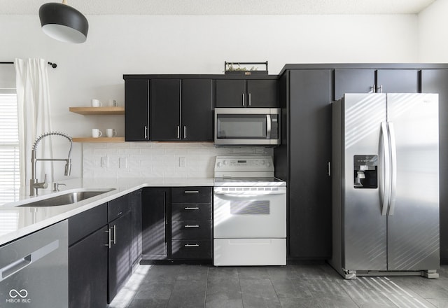 kitchen featuring a sink, open shelves, appliances with stainless steel finishes, light countertops, and dark cabinets