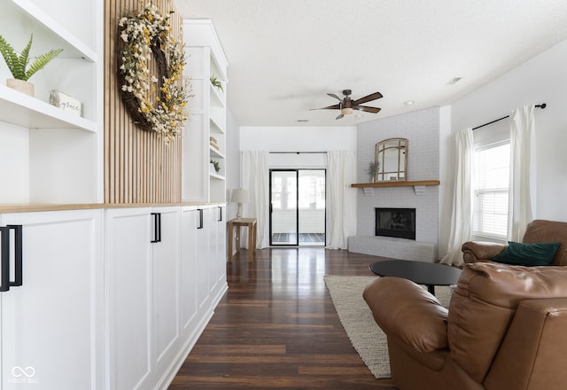 living area featuring built in shelves, dark wood-type flooring, a brick fireplace, and a textured ceiling