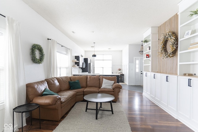 living area with dark wood-style floors, wainscoting, and a textured ceiling