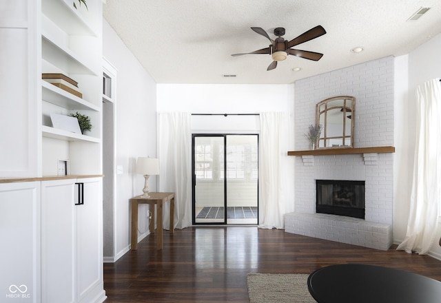 living area featuring a brick fireplace, visible vents, dark wood-style flooring, and a textured ceiling