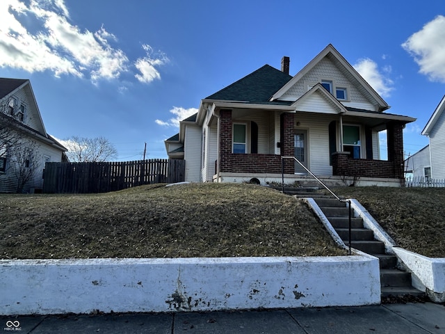 view of front of house featuring brick siding, covered porch, a chimney, and fence