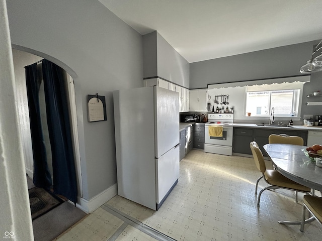 kitchen with a sink, white appliances, arched walkways, white cabinets, and light floors