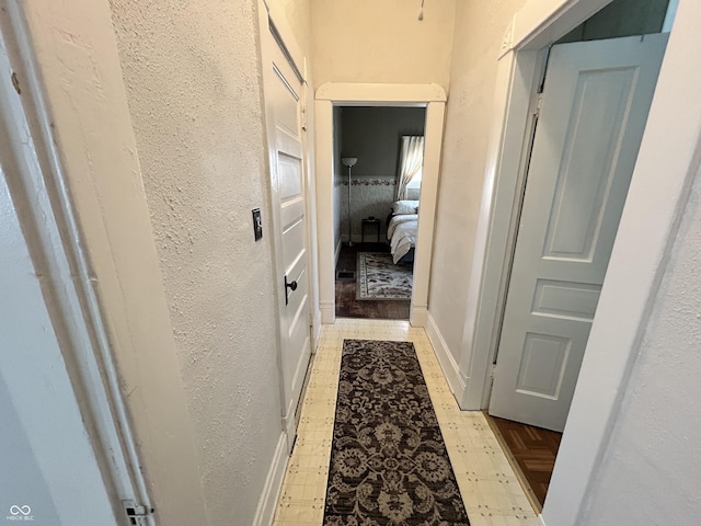 hall with tile patterned floors, baseboards, and a textured wall