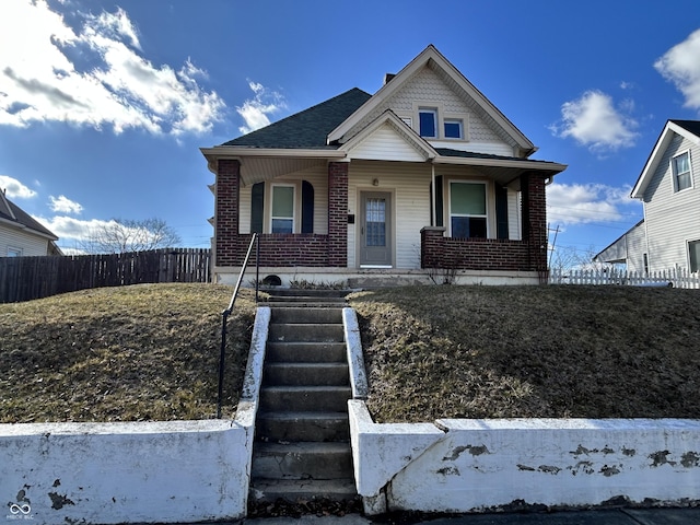 bungalow with brick siding, covered porch, a shingled roof, and fence