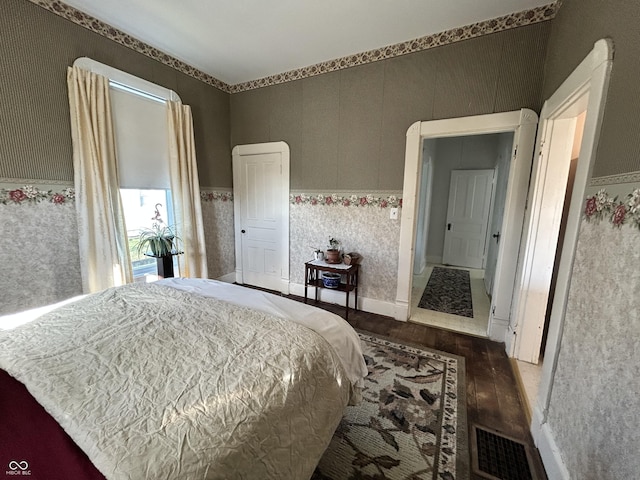 bedroom with visible vents, wallpapered walls, baseboards, and wood finished floors