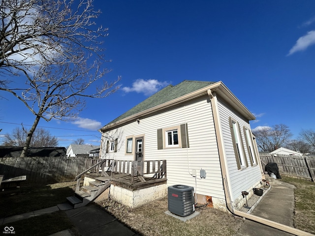 view of property exterior with central AC unit, a fenced backyard, and a shingled roof