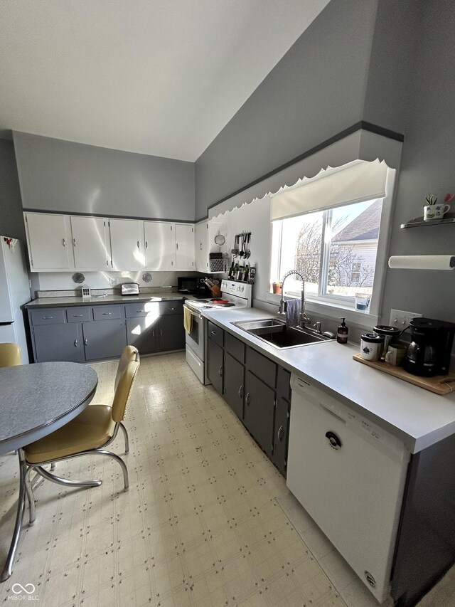 kitchen with a sink, white cabinetry, white appliances, lofted ceiling, and light floors