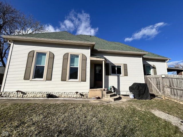 view of front facade featuring roof with shingles, a front lawn, and fence