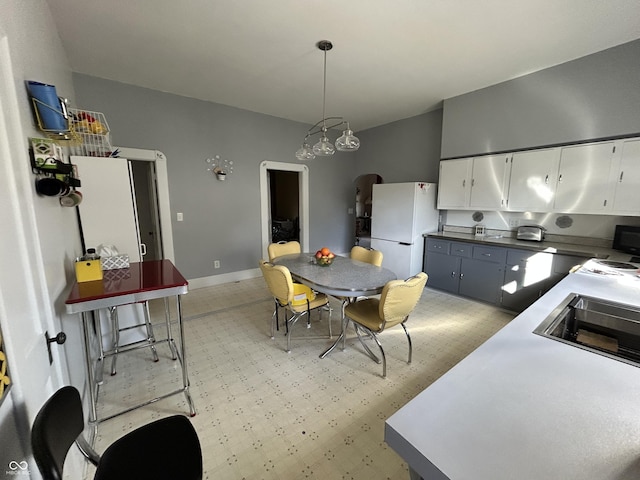 interior space with white cabinetry, freestanding refrigerator, baseboards, light floors, and hanging light fixtures