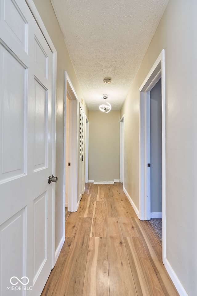 hallway featuring baseboards, light wood finished floors, and a textured ceiling