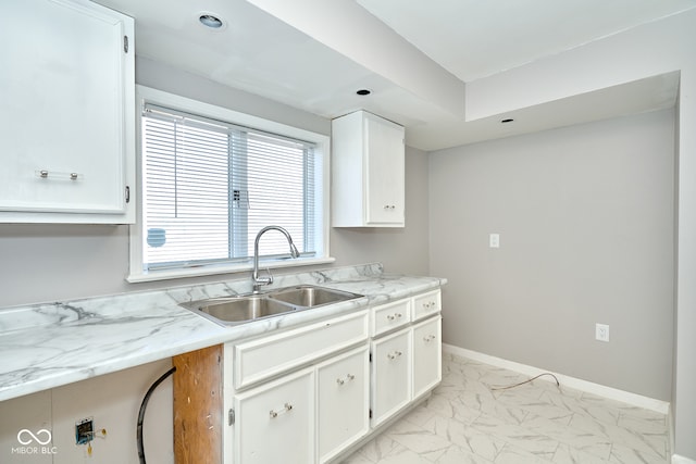 kitchen with marble finish floor, white cabinetry, baseboards, and a sink