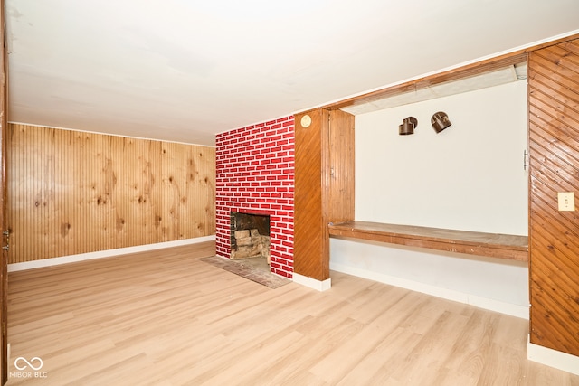 unfurnished living room with wooden walls, a brick fireplace, baseboards, and wood finished floors