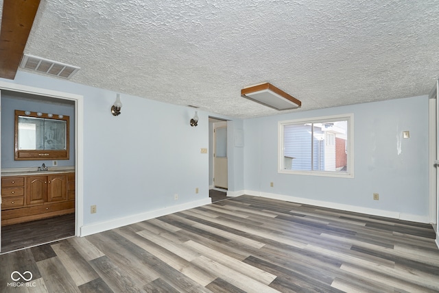 spare room featuring a textured ceiling, wood finished floors, visible vents, and a sink