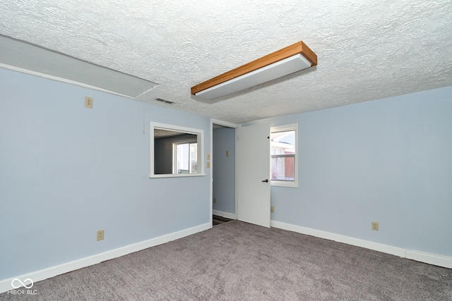 carpeted empty room featuring attic access, baseboards, visible vents, and a textured ceiling