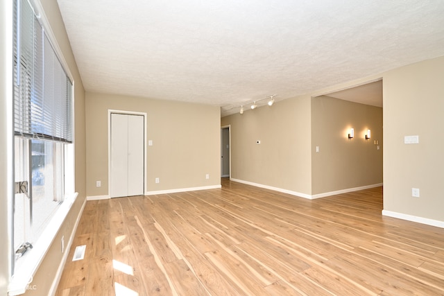 spare room featuring visible vents, light wood-style flooring, track lighting, a textured ceiling, and baseboards