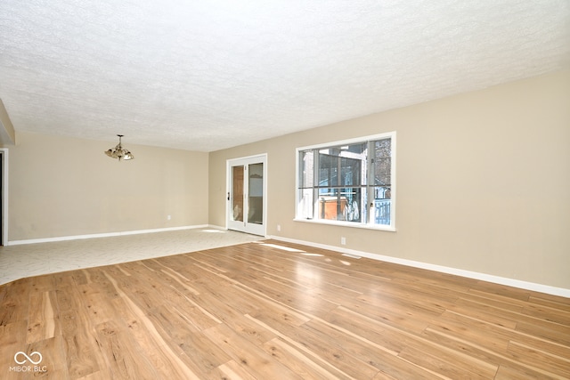 unfurnished room with light wood-type flooring, baseboards, a textured ceiling, and an inviting chandelier