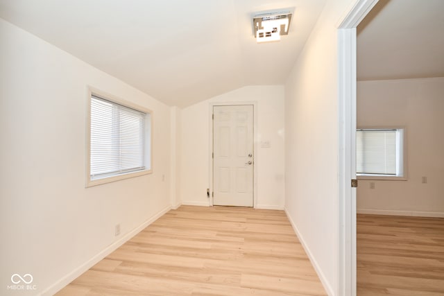 hall with baseboards, lofted ceiling, and light wood finished floors