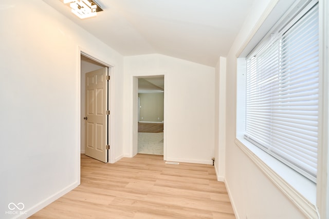 corridor featuring vaulted ceiling, light wood-style floors, and baseboards