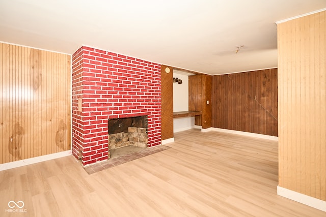 unfurnished living room featuring wood walls, a brick fireplace, baseboards, and wood finished floors