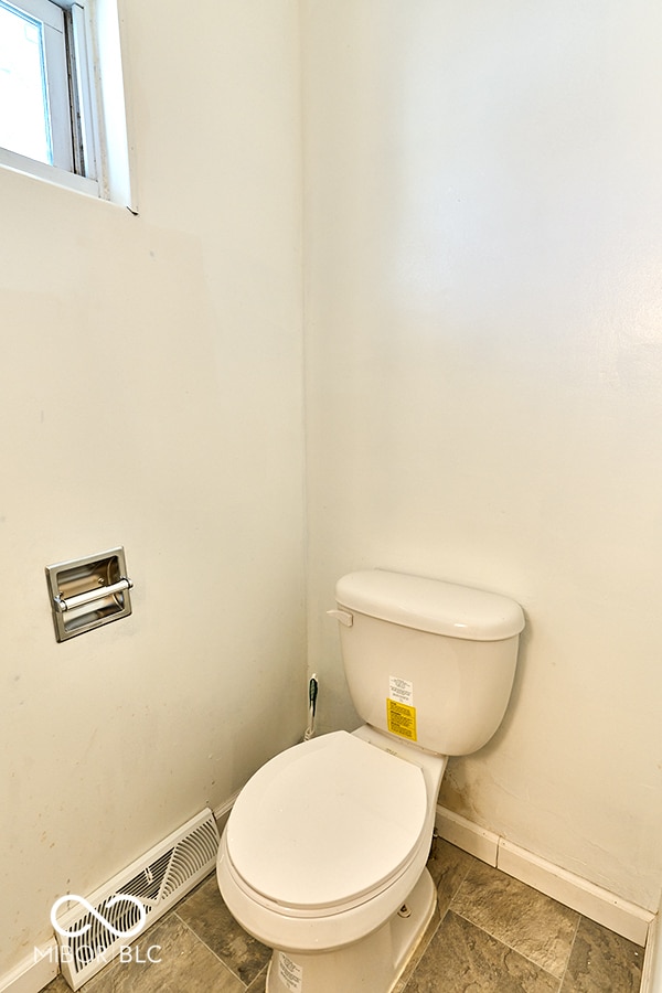 bathroom featuring stone finish floor, toilet, baseboards, and visible vents