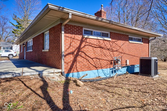 view of side of home with central AC unit, brick siding, and a chimney