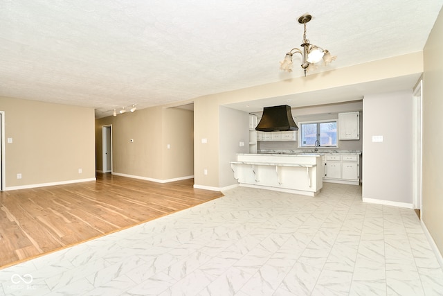 unfurnished living room with a notable chandelier, baseboards, marble finish floor, and a textured ceiling